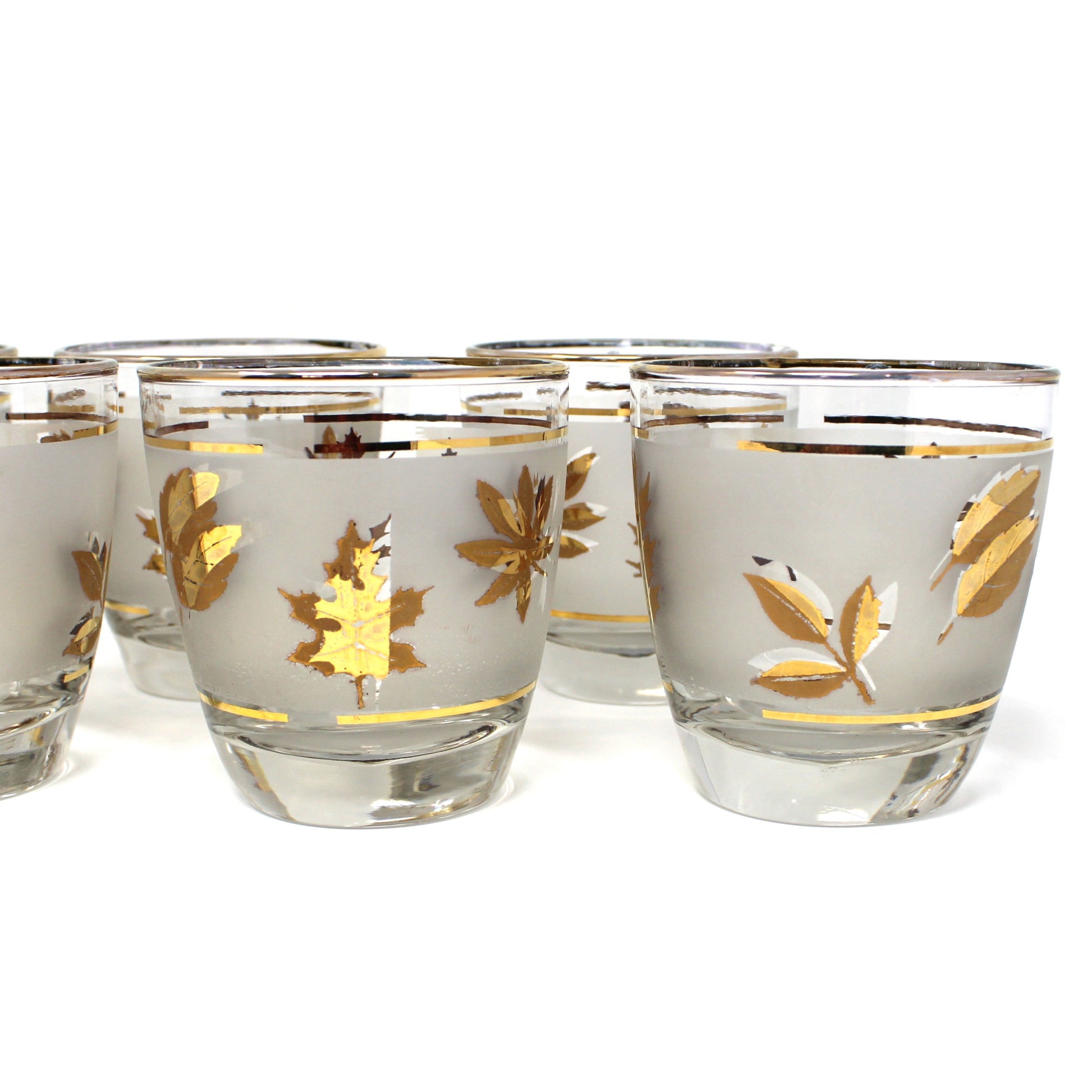 Set of six glass shot glasses with gold leaf design on a white background