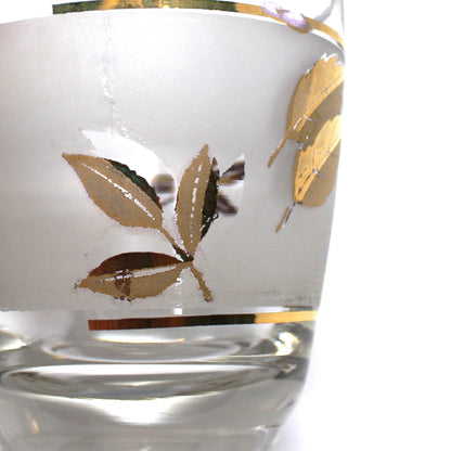 Hand holding a glass with gold leaf design on a white surface with more glasses in the background.