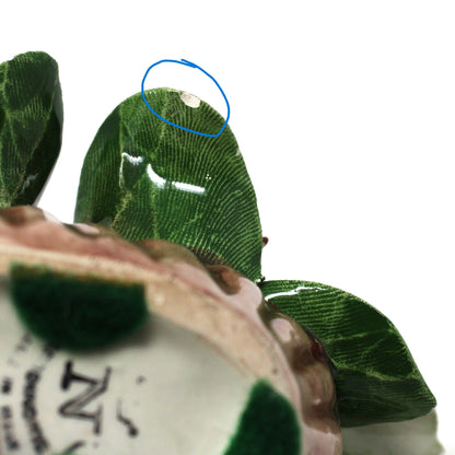 Close-up of a decorative item with green leaves and a shell, held by a hand.