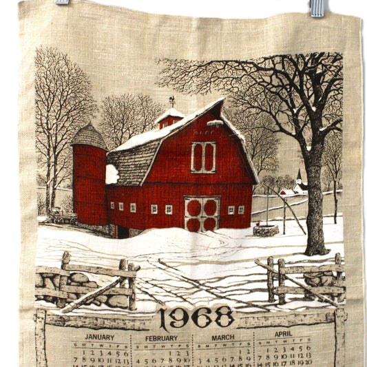 Fabric calendar with a red barn design and year 1968 printed on it, hanging on a wooden hanger.