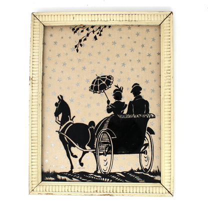 Framed silhouette artwork of a horse-drawn carriage with two figures on a white background with silver foil stars.