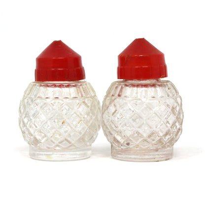 A pair of vintage glass salt or pepper shakers with red bakelite tops, displaying a diamond pattern design.