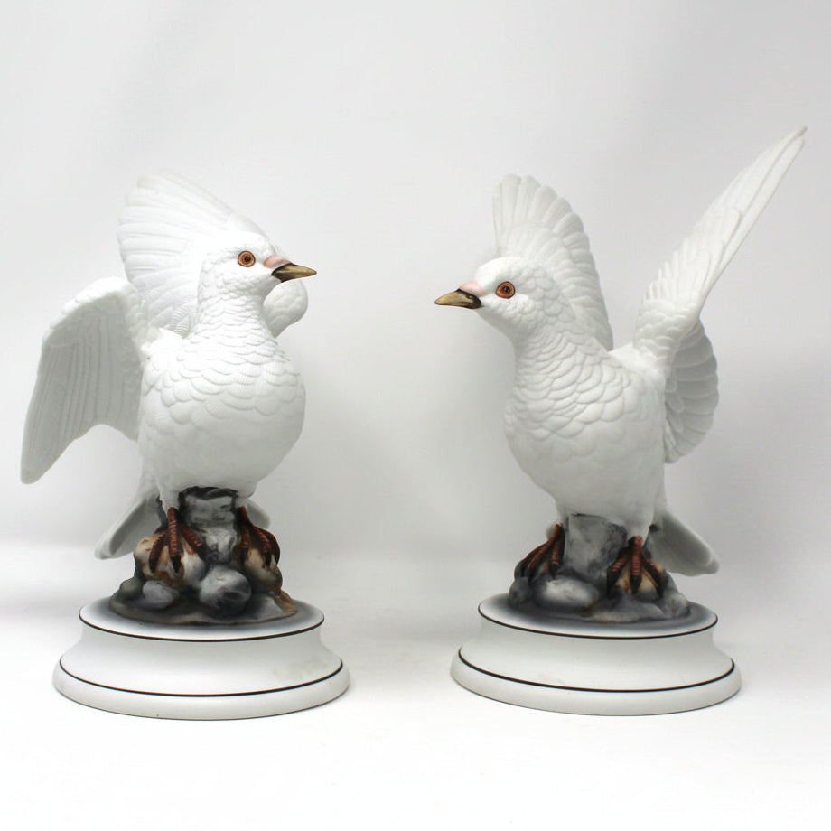 Two white ceramic bird figurines on gray stands against a white background