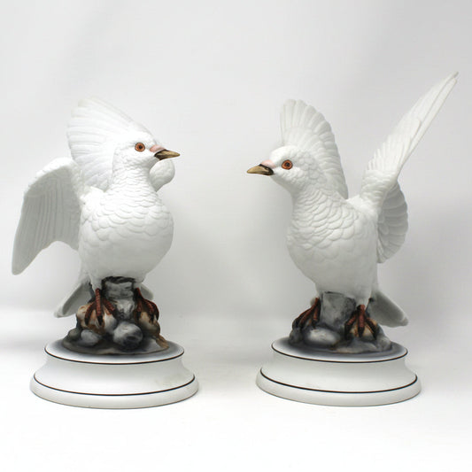Two white ceramic bird figurines on gray stands against a white background