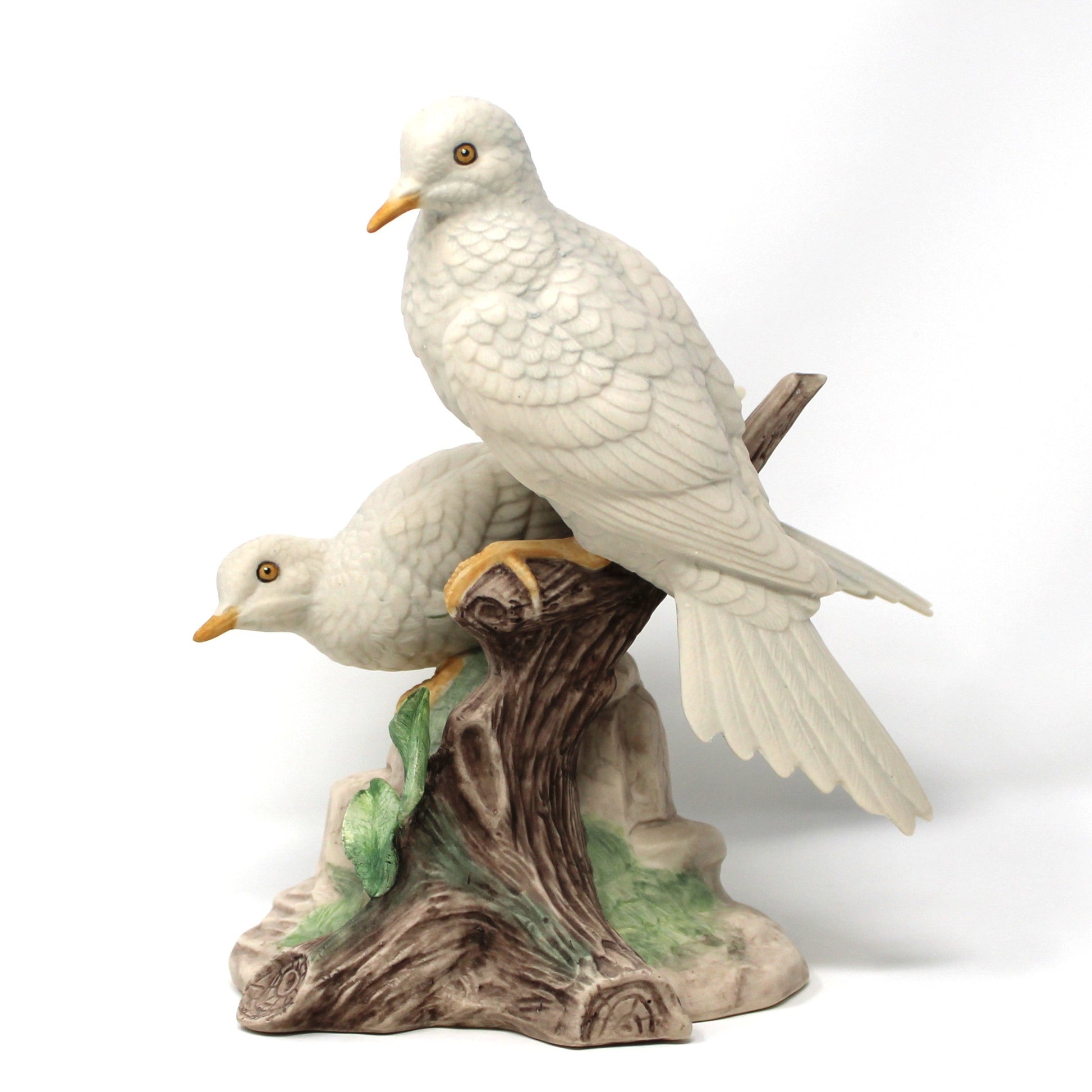 A vintage bisque porcelain figurine of two white doves perched on a brown and green textured tree stump base.