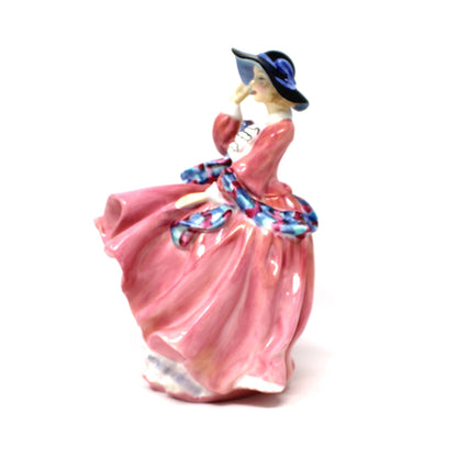 Side view of A vintage porcelain Royal Doulton figurine titled "Top O' The Hill". HN1849, of a woman in a flowing pink dress with blue hat.