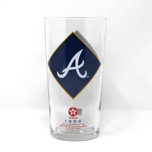 A clear glass beer pint glass featuring the Atlanta Braves logo, with a navy blue diamond on the front displaying a white script letter 'A' and a gold outline, plus a small red and white Texaco star logo near the base.