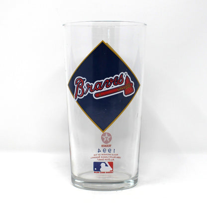 A vintage clear beer glass tumbler featuring a large navy blue diamond graphic with the Atlanta Braves logo in red and white, and a small MLB mark near the bottom. 1994