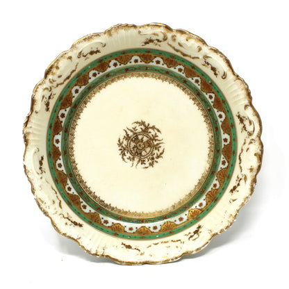 An antique ceramic plate with a scalloped rim, featuring a cream-colored center decorated with a brown floral motif, surrounded by a green and brown patterned border.