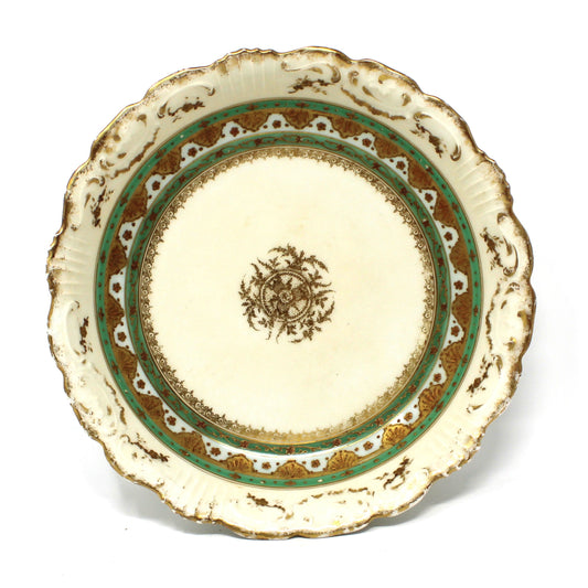 An antique ceramic plate with a scalloped rim, featuring a cream-colored center decorated with a brown floral motif, surrounded by a green and brown patterned border.