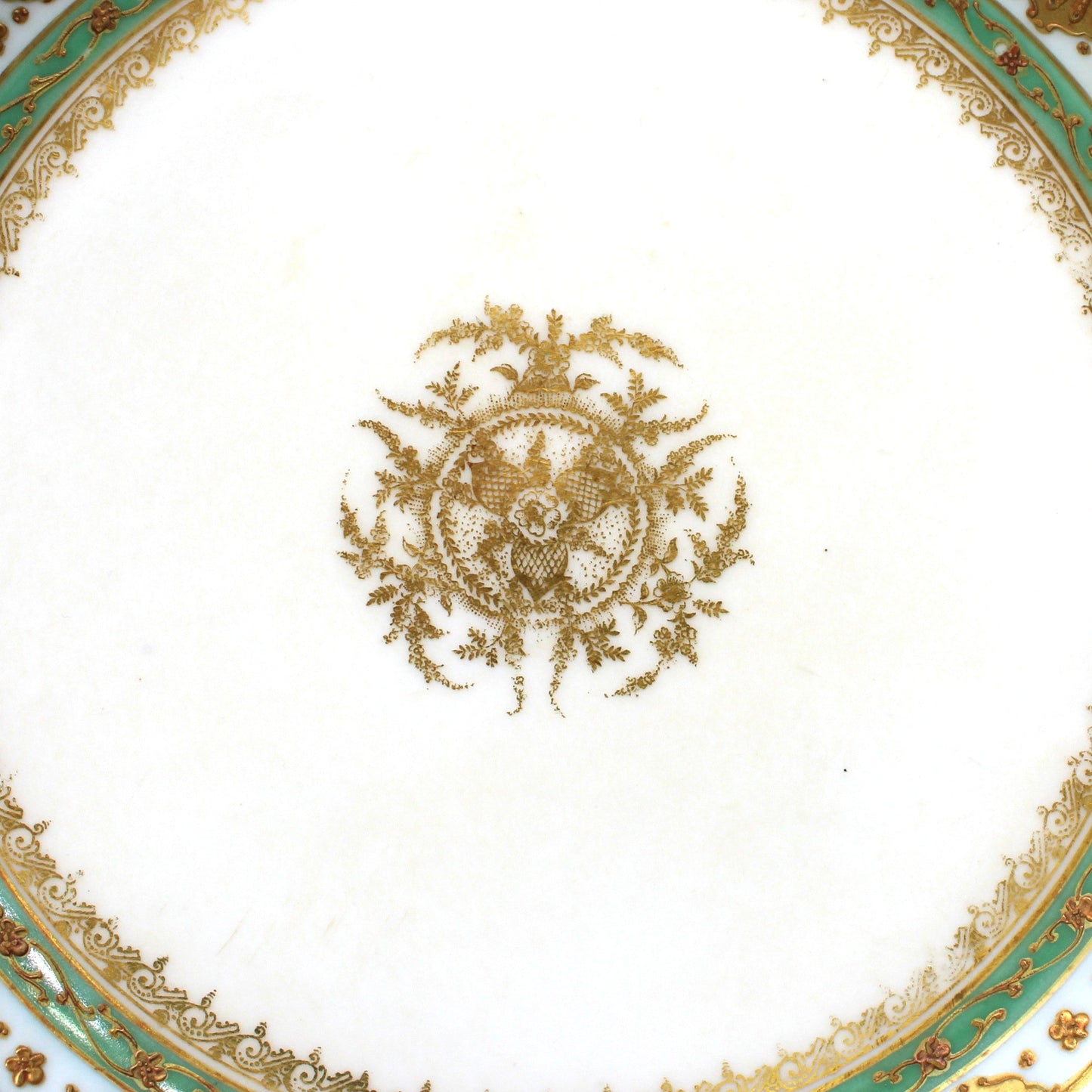 An ornate white porcelain bowl with a scalloped rim, decorated with intricate gold filigree, a central gold crest, and concentric rings of green and gold detailing.