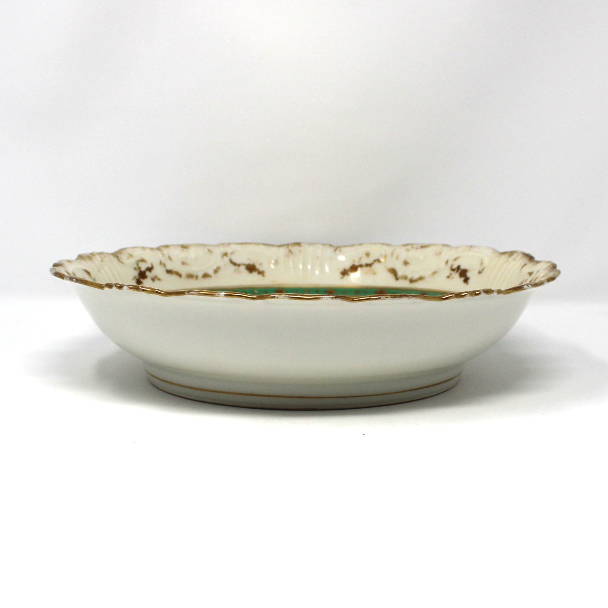 A Victorian cabinet porcelain bowl with a scalloped rim, featuring an off-white glaze, gold speckled detailing, and a thin green stripe near the edge.