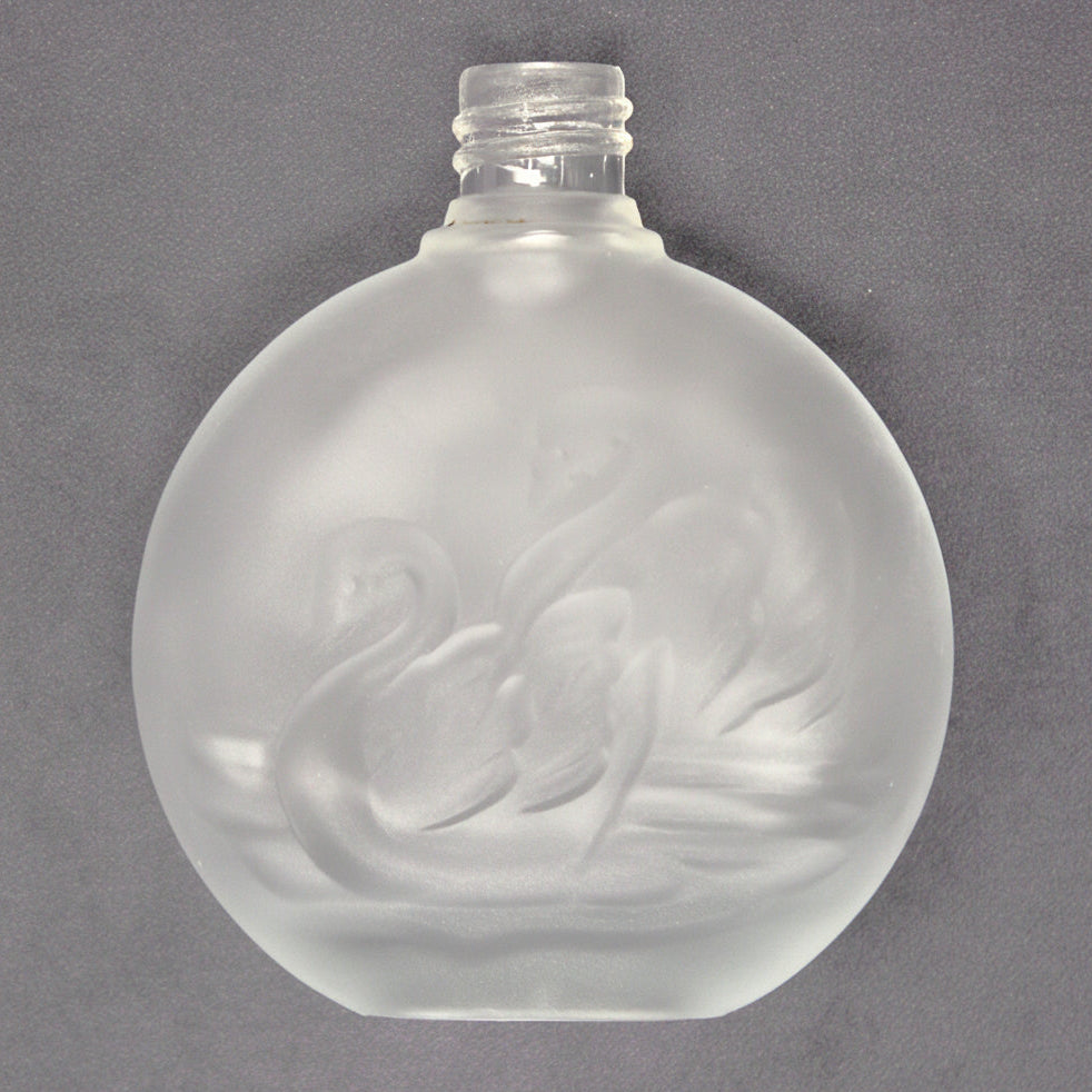 A vintage perfume bottle, clear frosted glass with a double swan motif embossed on the front