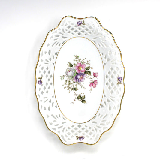 A vintage oval white porcelain decorative bowl with a cutout lattice border, gold trim, and a central floral motif featuring pink, purple, and green roses.  Schumann Arzberg, Bavaria, Germany.