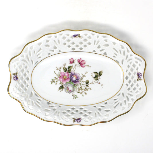 A vintage Schumann Arzberg, Bavaria, Germany porcelain oval bowl.  White porcelain with an intricate openwork cutout border, a central floral bouquet of pink, purple, and green flowers, and accented with a gold rim.