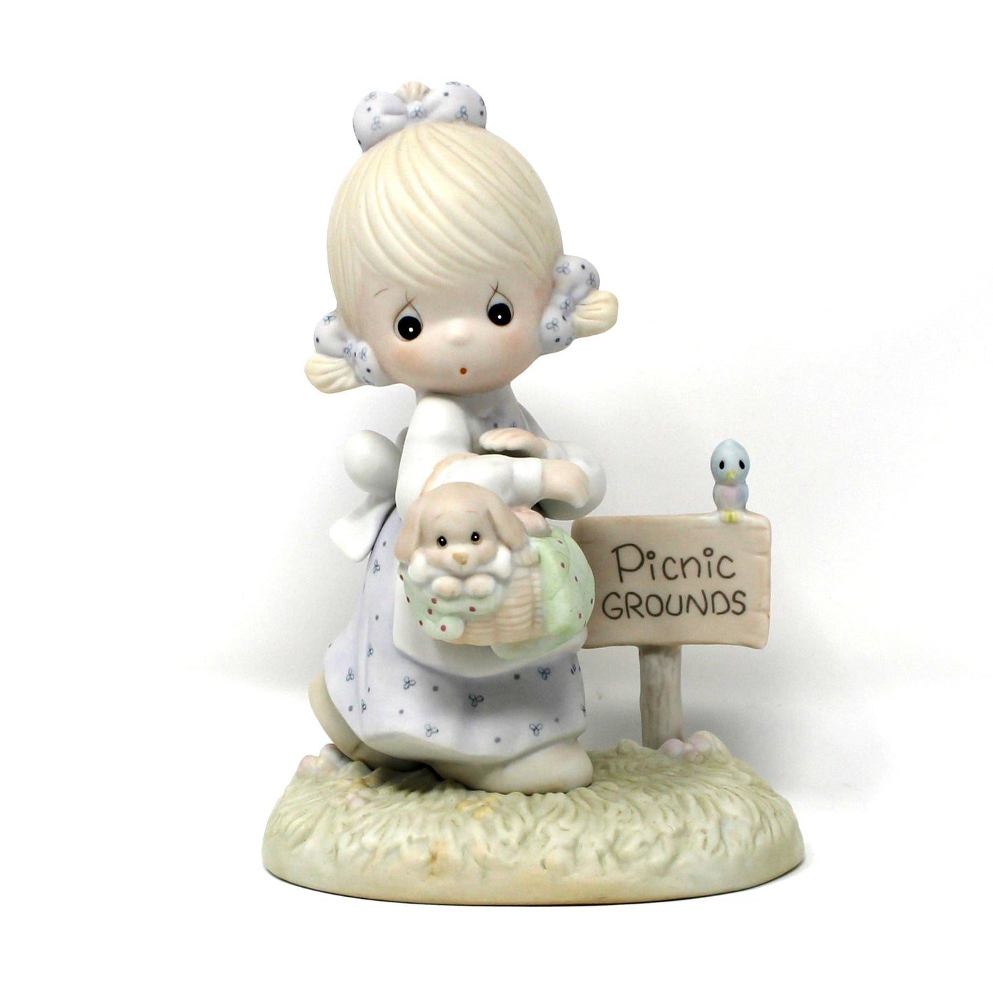 A vintage Precious Moments figurine from the Calendar Girls collection, titled July.  A young girl in a white dress holding a basket, next to a small sign "Picnic Grounds".  Dated 1992 (clef note).