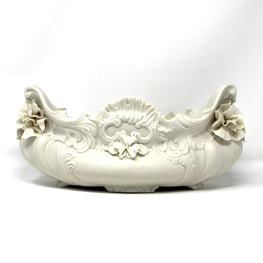 A vintage, ornate, white ceramic Italian oval planter with sculpted floral details and a decorative rim. Marked Italy for Bonwit Teller