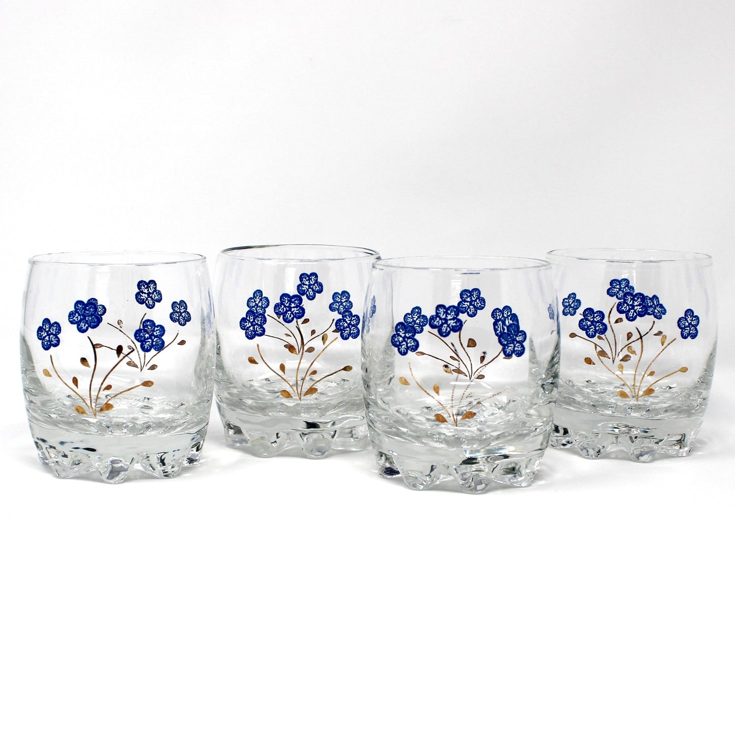 Four clear glass tumblers with a textured base, decorated with blue floral patterns and gold stems