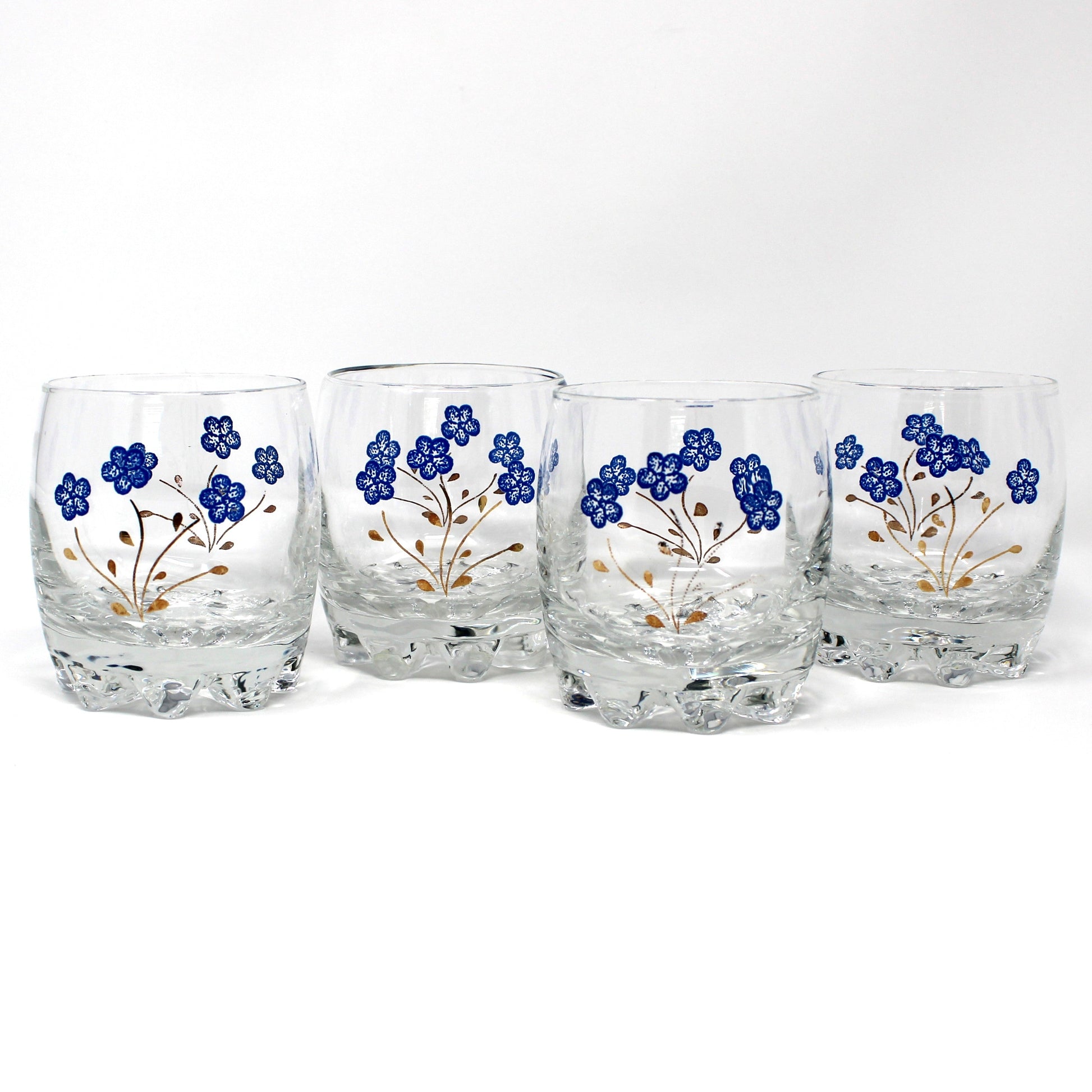 Four clear glass tumblers with a textured base, decorated with blue floral patterns and gold stems