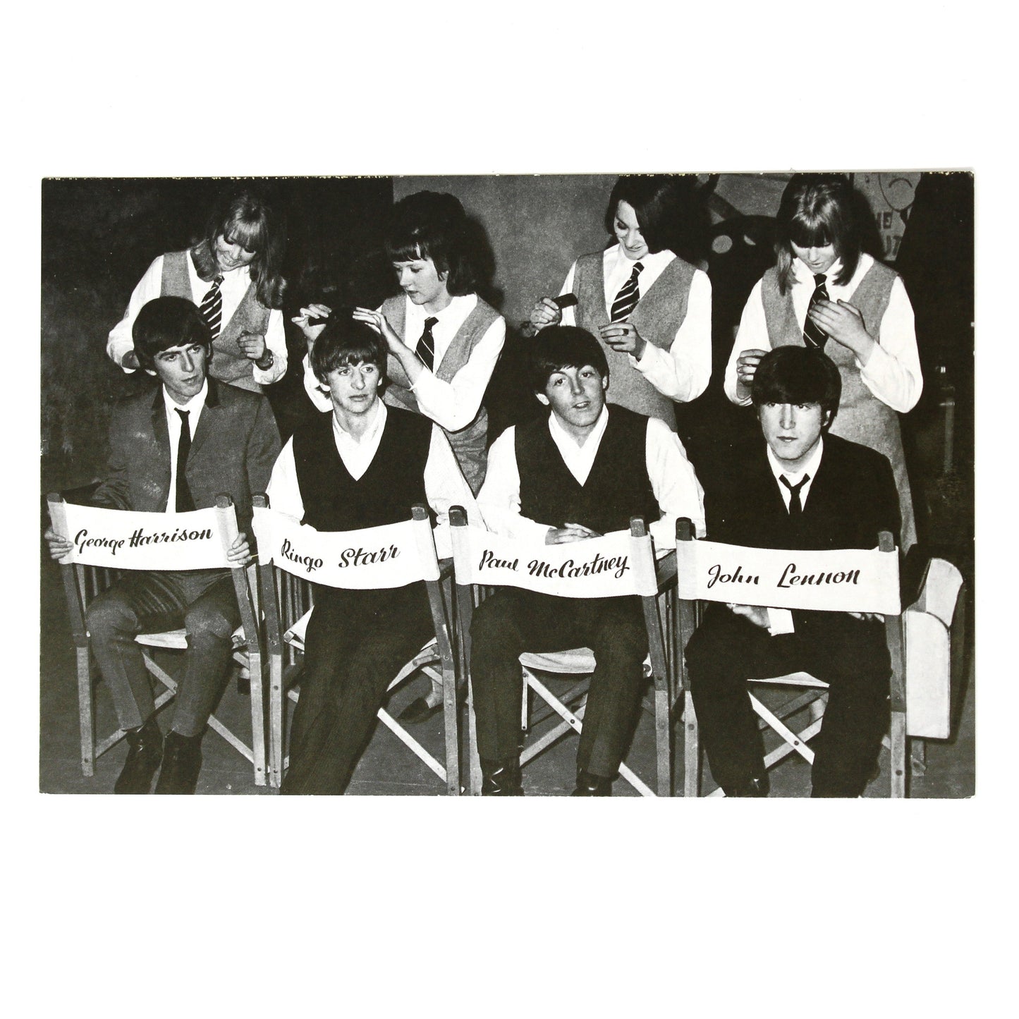 A black and white vintage postcard depicting the Beatles seated in chairs, with their names: 'John Lennon', 'Paul McCartney', 'George Harrison', and 'Ringo Starr'.