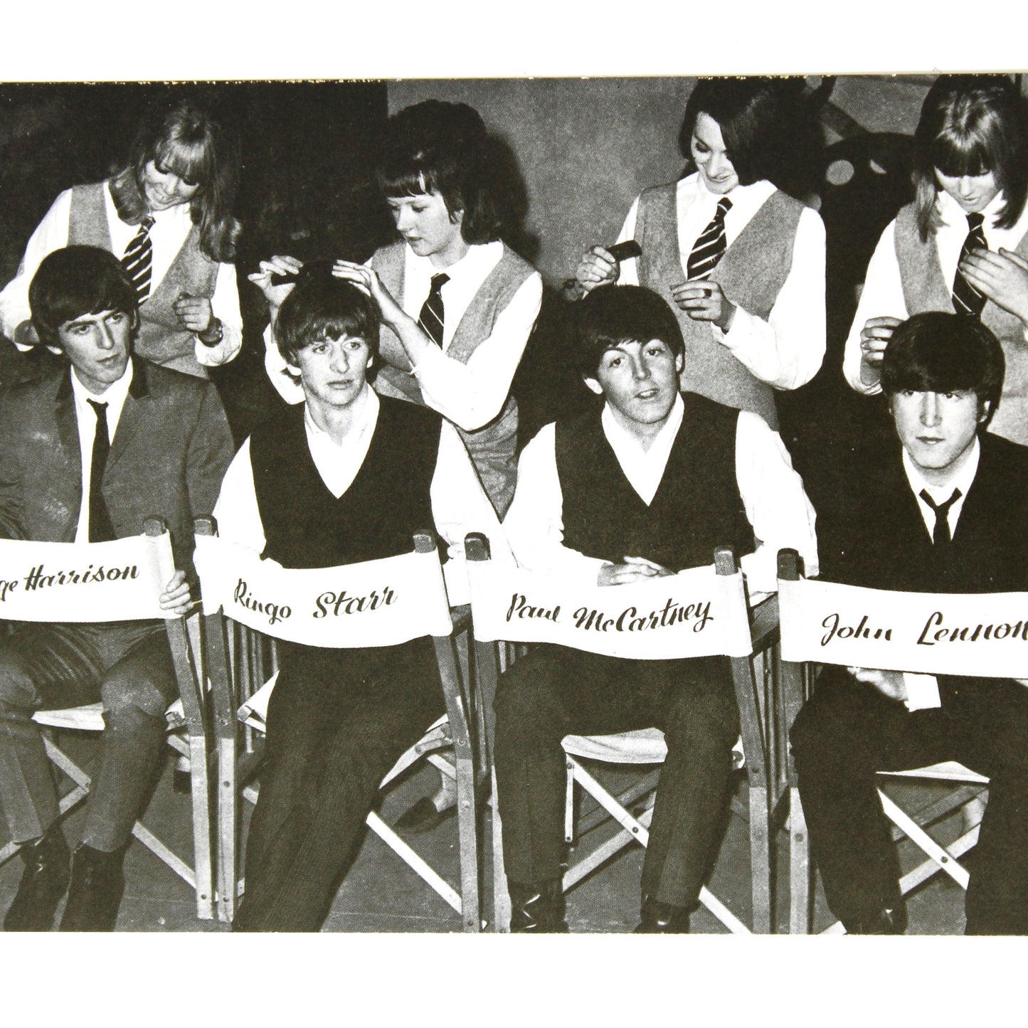 A vintage black and white postcard depicting the band The Beatles seated in chairs with their names: George Harrison, George McCartney, Ringo Starr, and John Lennon.