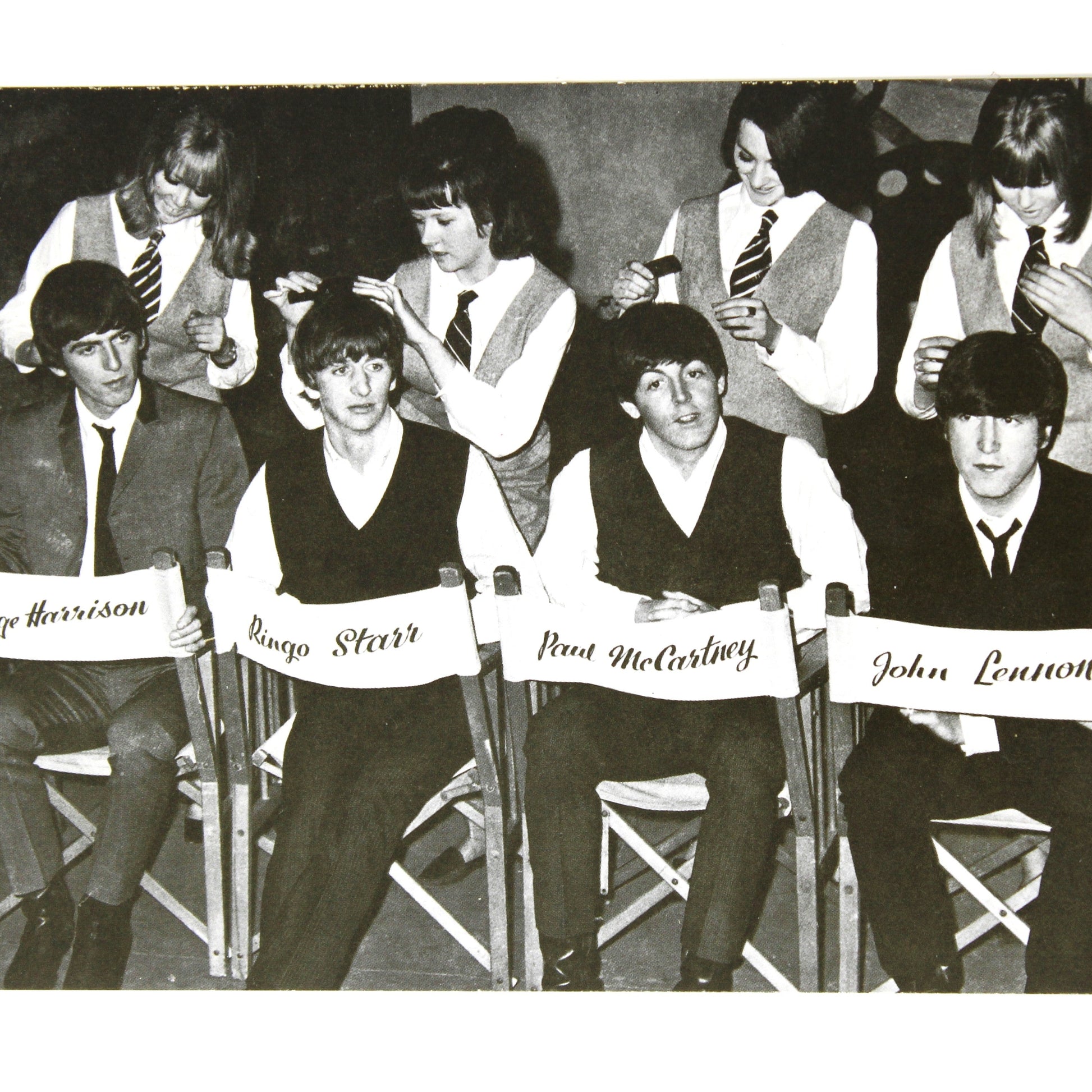A vintage black and white postcard depicting the band The Beatles seated in chairs with their names: George Harrison, George McCartney, Ringo Starr, and John Lennon.