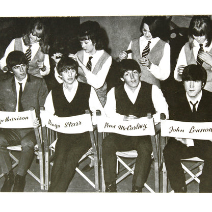 A vintage black and white postcard depicting the band The Beatles seated in chairs with their names: George Harrison, George McCartney, Ringo Starr, and John Lennon.