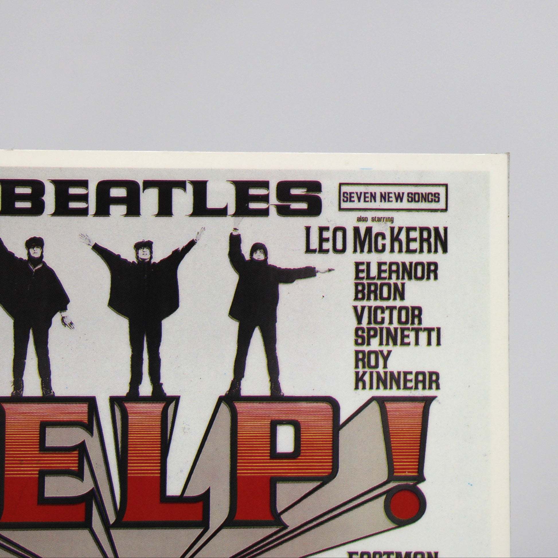A close-up of a vintage Beatles 'Help!' postcard, showing the silhouettes of the band members and large red-and-white 'HELP!' text