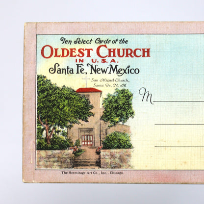 A vintage collectible postcard from Santa Fe, New Mexico, held by a hand against a plain white background. The postcard features an illustration of the Oldest Church in Santa Fe and has text reading 'Ten Select Cards of the Oldest Church in U.