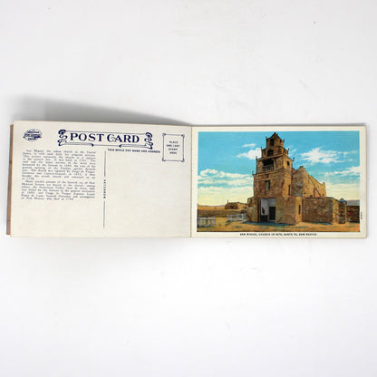 An open vintage postcard showing the front and back, with a printed photograph of a historic stone building on the right and postcard text on the left, photographed on a white background.