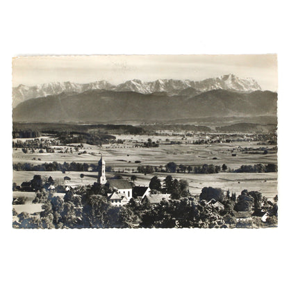 A vintage black and white landscape postcard with real photograph by Perutz film.  Featuring a town with a church steeple in the foreground and a snow-capped mountain range in the background.