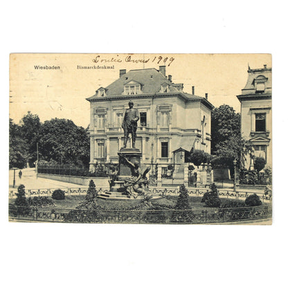 Antique black and white postcard depicting a grand neoclassical building with a central statue and manicured gardens. Travel postcard, Germany