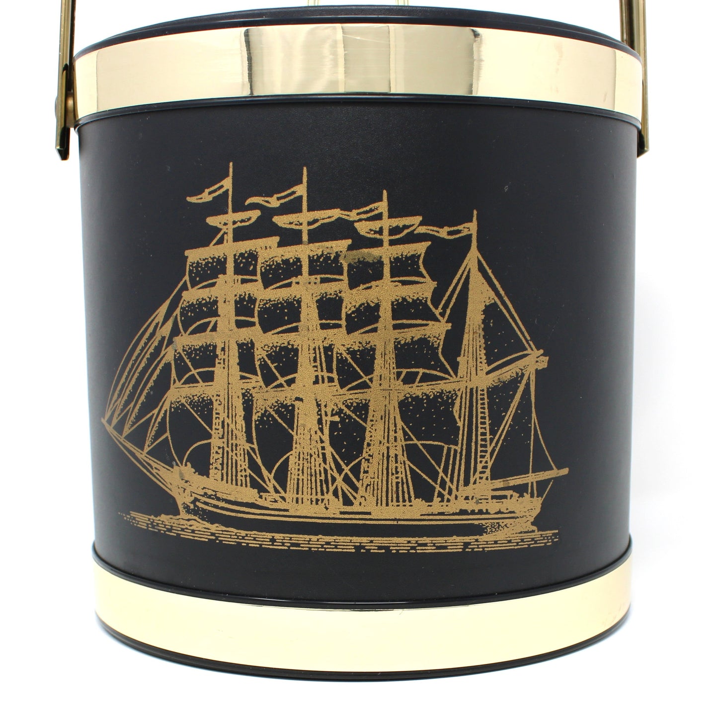 Close up of a vintage ice bucket, black cylindrical bucket-style with a gold-toned handle and trim, featuring a gold ship illustration on the front