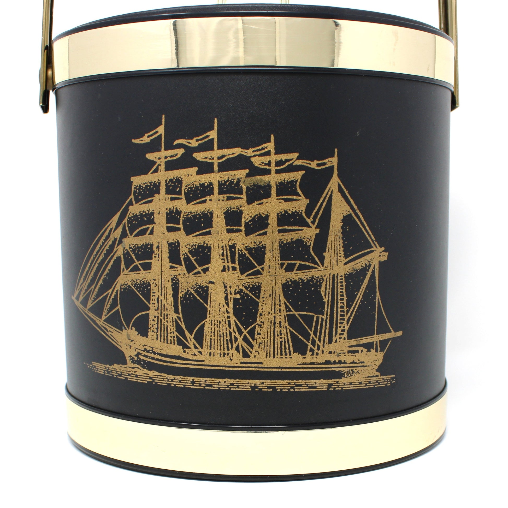Close up of a vintage ice bucket, black cylindrical bucket-style with a gold-toned handle and trim, featuring a gold ship illustration on the front