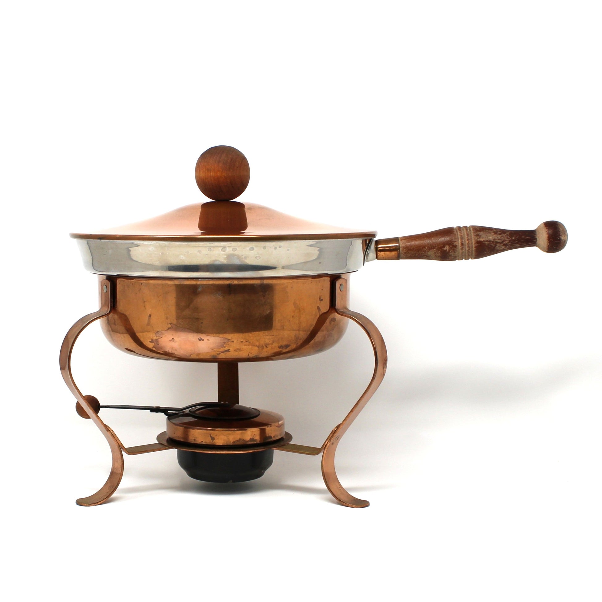 A vintage copper chafing dish with a wooden handle and lid knob, resting on a matching copper tripod burner with a small black fuel pan