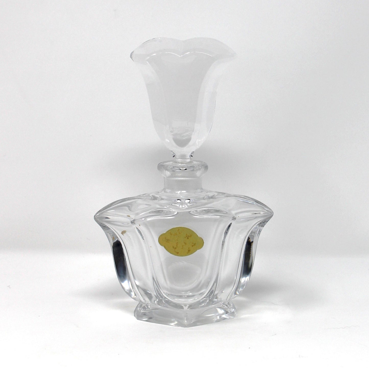 A clear glass decanter with a faceted, ribbed base and a flared stopper, shown on a plain white studio background with a small gold sticker on the front.