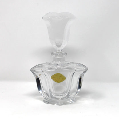 A clear glass decanter with a faceted, ribbed base and a flared stopper, shown on a plain white studio background with a small gold sticker on the front.