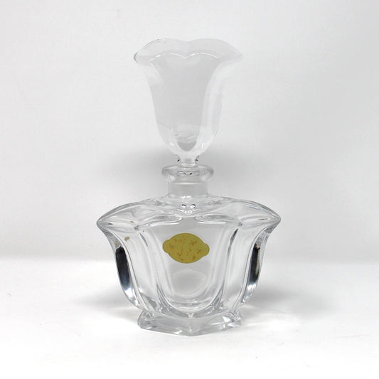 A clear glass decanter with a faceted, ribbed base and a flared stopper, shown on a plain white studio background with a small gold sticker on the front.