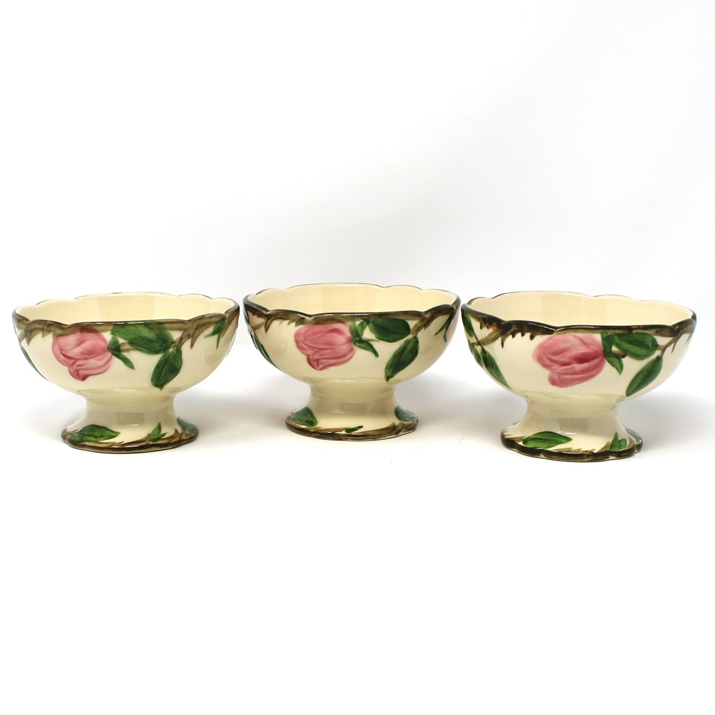 Back view of three vintage Franciscan Desert Rose ceramic footed bowls with pink rose and green leaf patterns on a cream background.