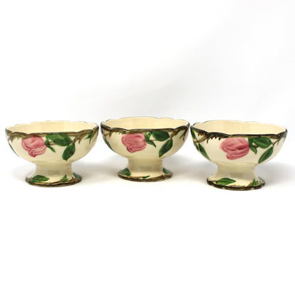 Back view of three vintage Franciscan Desert Rose ceramic footed bowls with pink rose and green leaf patterns on a cream background.