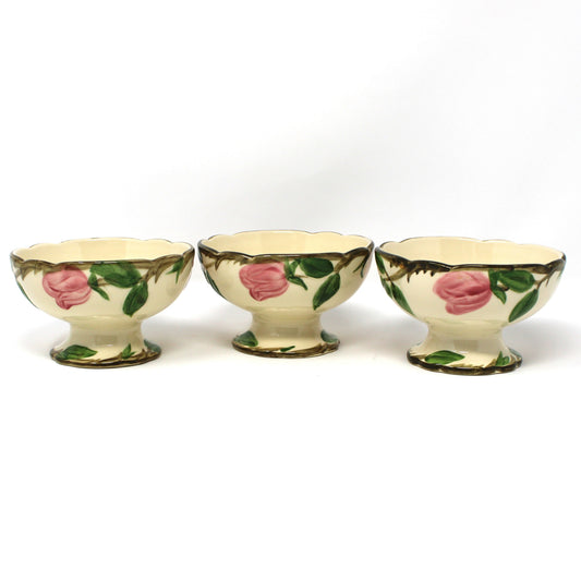Back view of three vintage Franciscan Desert Rose ceramic footed bowls with pink rose and green leaf patterns on a cream background.