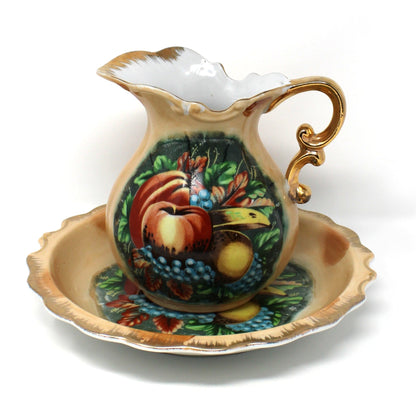 A vintage ceramic pitcher and basin set with hand-painted fruit motifs, including red apples, yellow pears, and blue grapes.