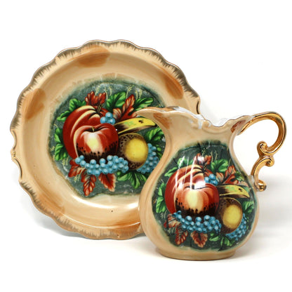 A vintage ceramic pitcher and basin set with hand-painted fruit motifs, including red apples, yellow pears, and blue grapes.