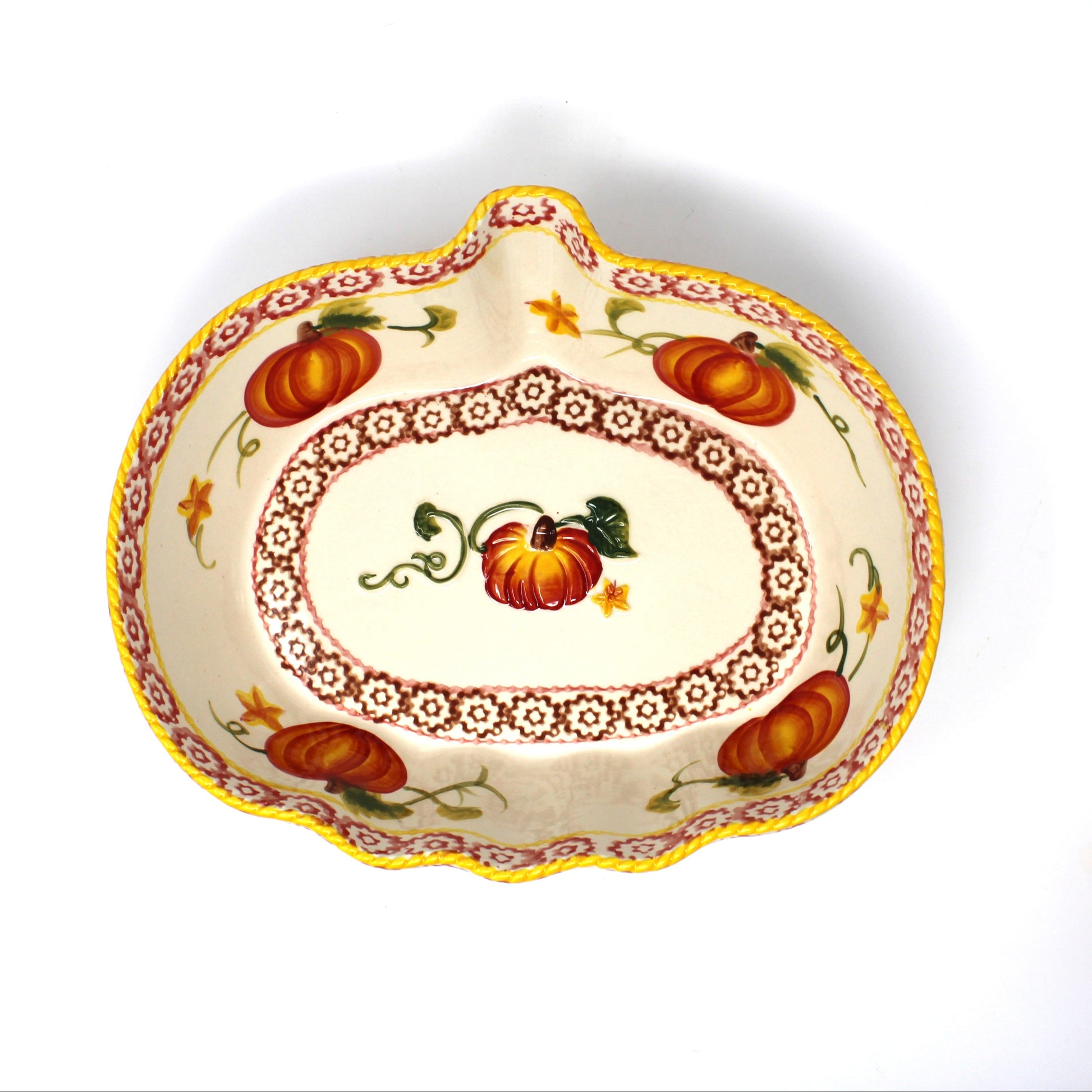 A decorative ceramic pumpkin-shaped serving dish with a hand-painted autumn design featuring pumpkins, leaves, and floral borders, shown on a white background with another dish partially visible on the right.