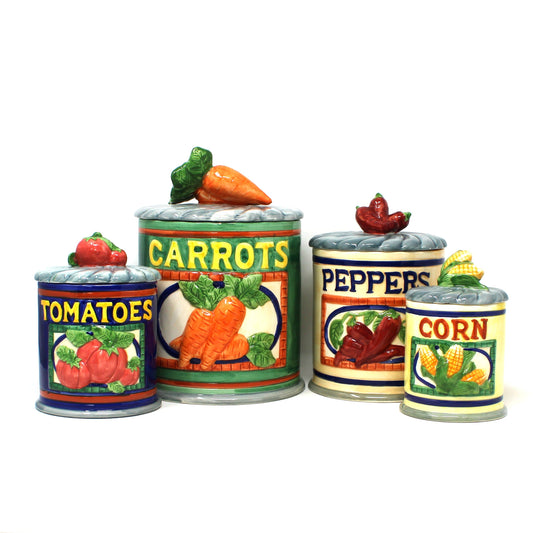 A vintage set of four ceramic canisters.  Mimicking can labels on the front, with lids shaped like vegetables, including tomatoes, carrots, peppers, and corn. Dated 1996 Jay Imports.