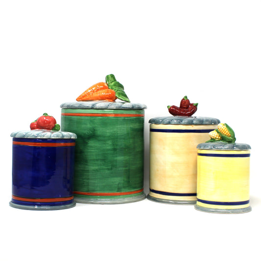 Back view of vintage set of four ceramic canisters.  Mimicking can labels on the front, with lids shaped like vegetables, including tomatoes, carrots, peppers, and corn. 