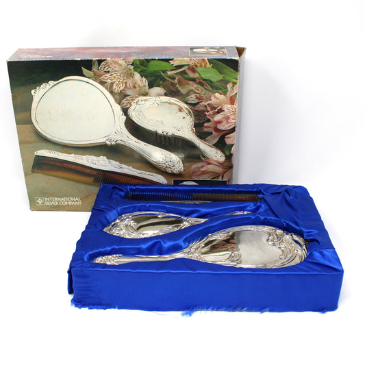 A vintage silverplate hand mirror set with brush and comb, ornate silver handles, from ISC in its original box.