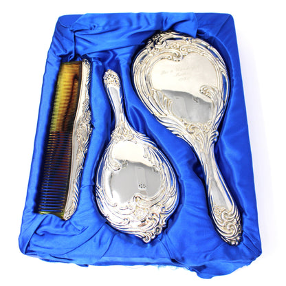 A vintage three-piece silver vanity set including a large hand mirror, a brush, and an ornate comb from ISC.