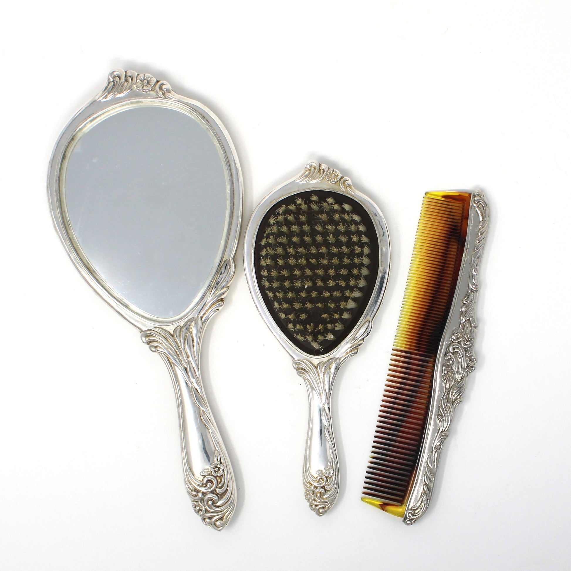 A vintage-style vanity set consisting of two ornate hand mirrors and a tortoiseshell hair comb with silver handles, displayed on a white background.