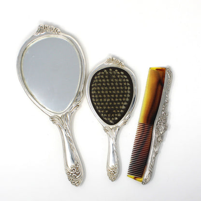 A vintage-style vanity set consisting of two ornate hand mirrors and a tortoiseshell hair comb with silver handles, displayed on a white background.